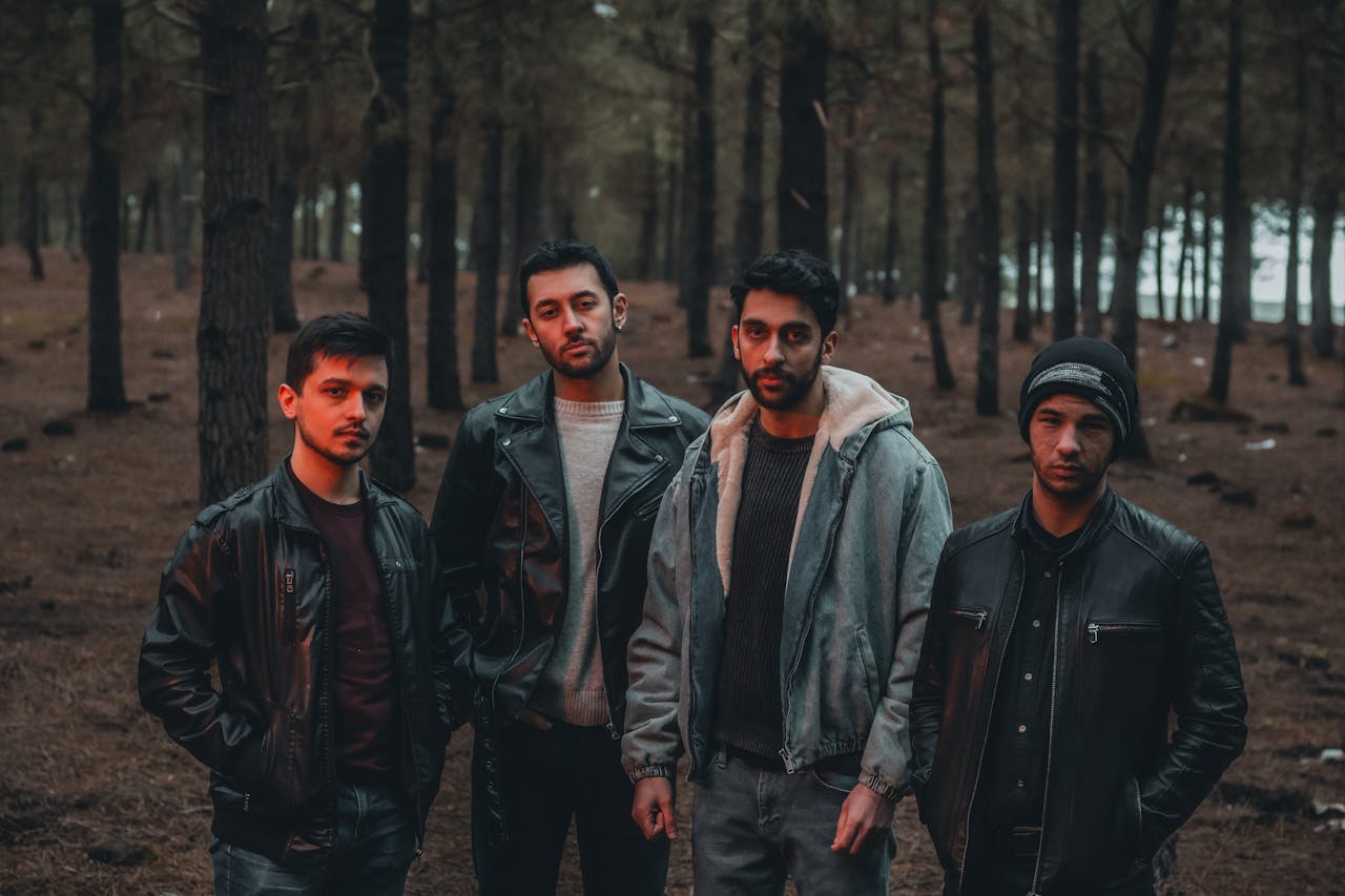 A group of men in stylish jackets posing confidently in a dense forest setting.