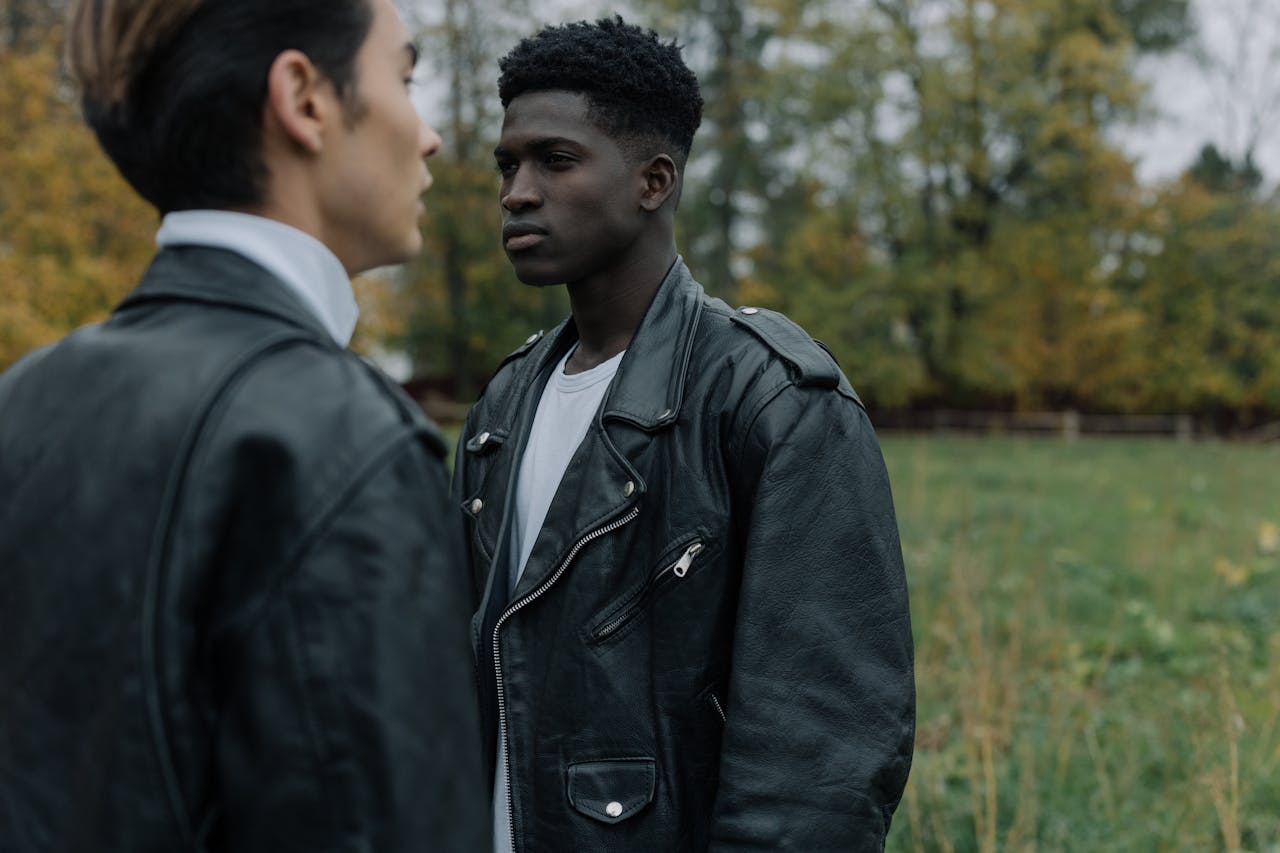 Two fashionable men wearing leather jackets in a serene outdoor setting.